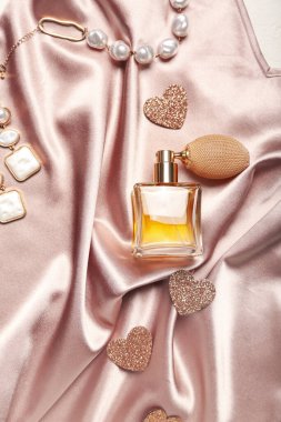 Perfume with jewelry and hearts for Valentine's day on silk clothes, closeup