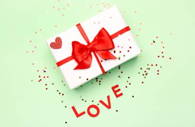 Gift box with beautiful bow and word LOVE on green background. Valentine's Day celebration