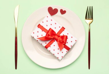 Table setting with gift box and hearts on green background. Valentine's Day celebration