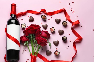 Composition with bottle of wine, rose flowers and chocolate candies on pink background. Valentine's Day celebration