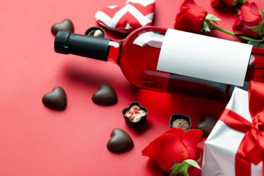 Bottle of wine, chocolate candies, rose flowers and gifts on red background. Valentine's Day celebration