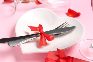 Heart shaped plate with cutlery on pink background, closeup. Valentine's Day celebration