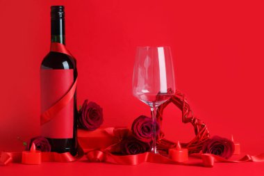 Composition with bottle of wine, glass, rose flowers and ribbon on red background. Valentine's Day celebration