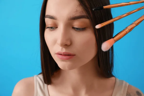 Young woman with makeup brushes on blue background, closeup