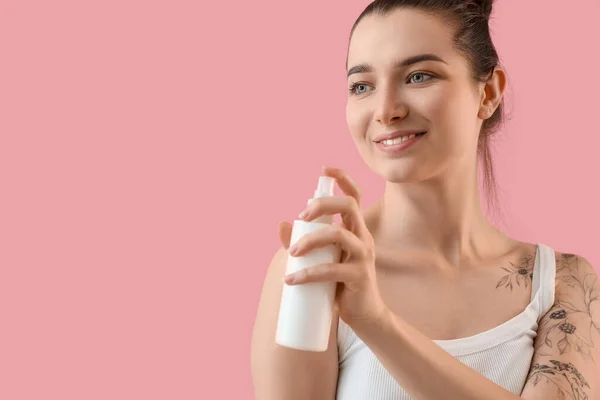 Young woman with cosmetic spray bottle on pink background, closeup