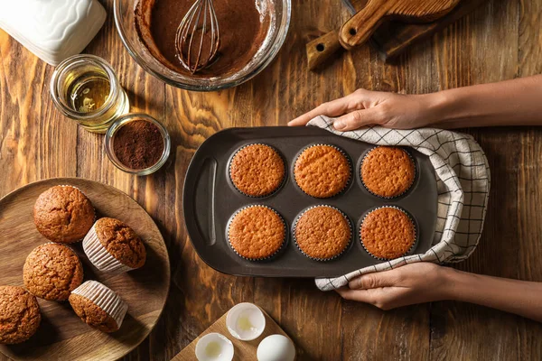 Female hands with tray of tasty muffins on wooden background