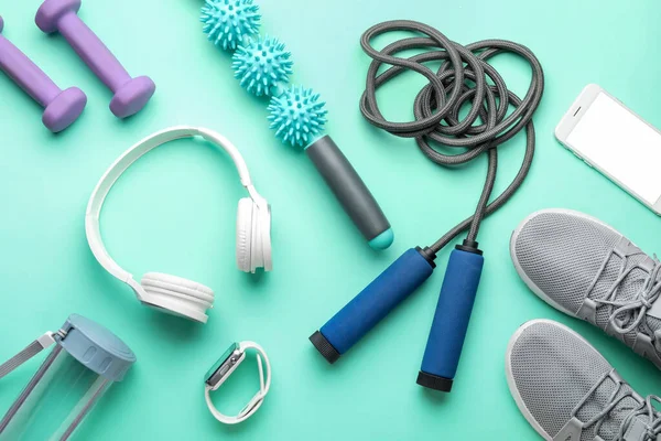 Skipping rope with sports equipment, headphones, bottle, sneakers and gadgets on green background