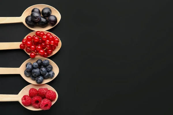 Wooden spoons with fresh berries on dark background