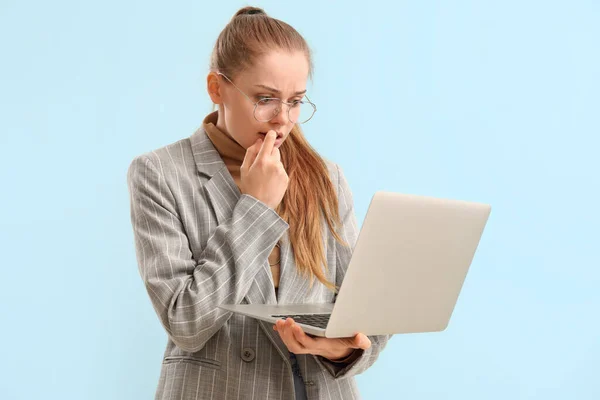 Young businesswoman with laptop biting nails on blue background