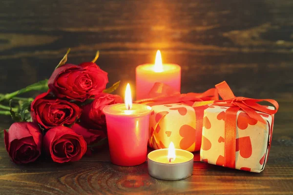 Burning candles, gift boxes and rose flowers on wooden background. Valentine\'s Day celebration
