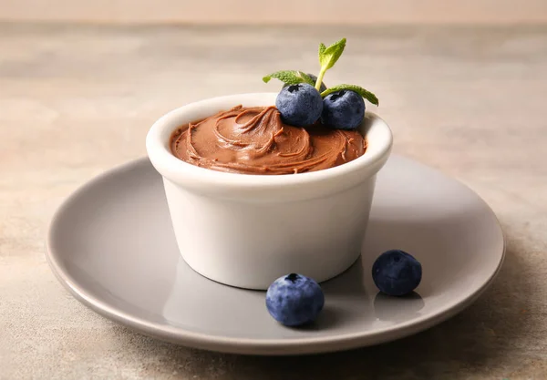 Plate with bowl of delicious chocolate pudding and blueberry on grey table