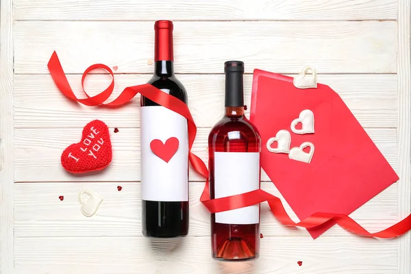 Bottles of wine, heart with text I LOVE YOU, envelope and ribbon on white wooden table. Valentine\'s Day celebration