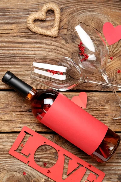 Bottle of wine, glasses, hearts and word LOVE on wooden background. Valentine\'s Day celebration