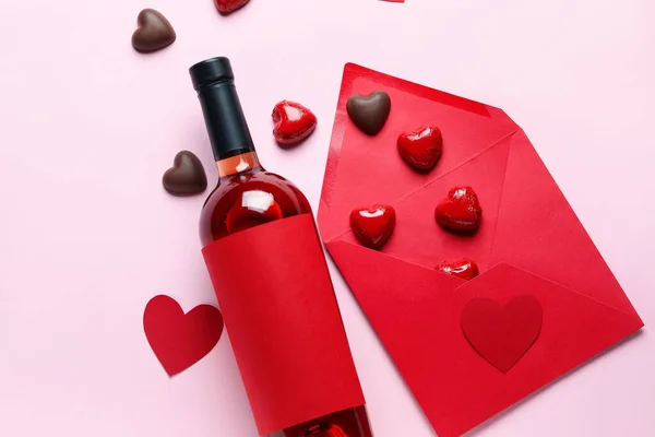 Bottle of wine, chocolate candies and envelope on pink background. Valentine\'s Day celebration