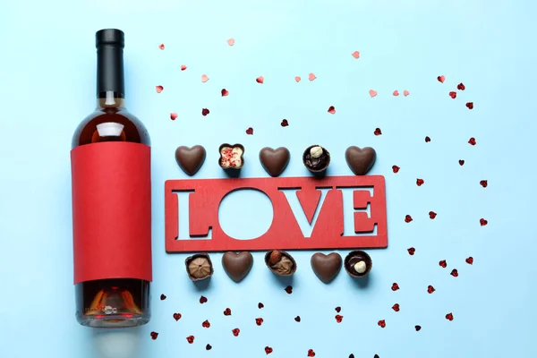 Bottle of wine, chocolate candies and word LOVE on blue background. Valentine\'s Day celebration