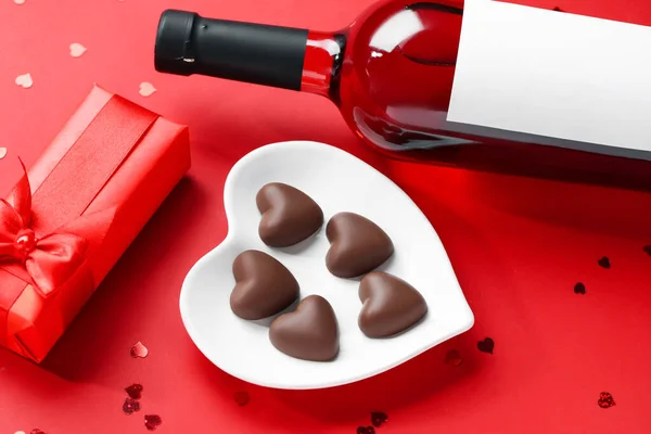 Bottle of wine, chocolate candies and gift box on red background. Valentine\'s Day celebration