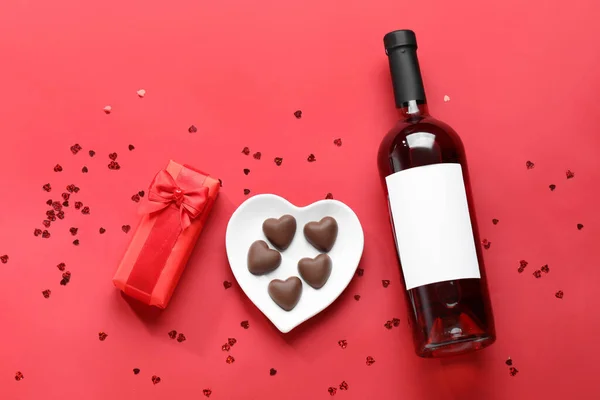 Bottle of wine, chocolate candies and gift box on red background. Valentine\'s Day celebration