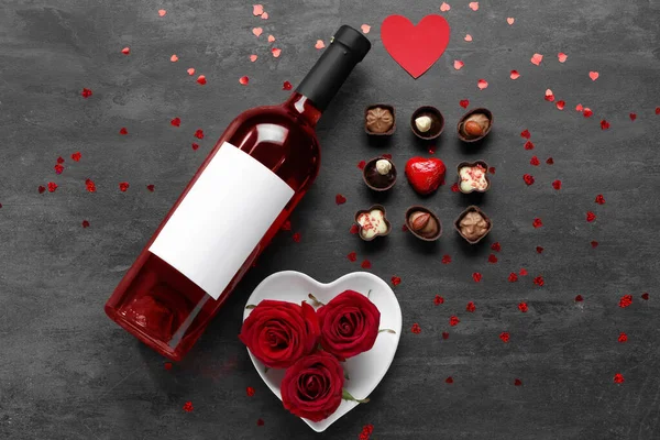 Bottle of wine, chocolate candies and rose flowers on black background. Valentine\'s Day celebration