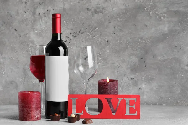 Glass of wine, bottle, word LOVE and burning candles on grey grunge background. Valentine's Day celebration