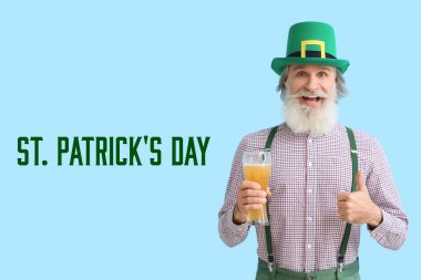 Senior man with glass of beer showing thumb-up on blue background. St. Patrick's Day celebration