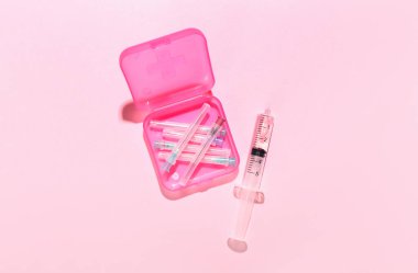 Medical syringe with remedy, container and needles on pink background