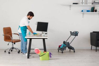 Male janitor cleaning desk in office