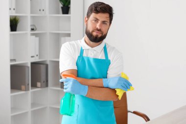 Male janitor with rag and detergent in office