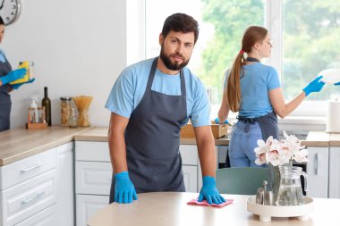 Male janitor cleaning dining table in kitchen