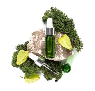 Cosmetic dropper bottles with green moss and rock on white background