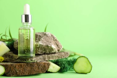 Cosmetic dropper bottle with green moss, cucumber and rocks on color background