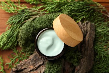 Jar of cream with green moss and tree bark on wooden background