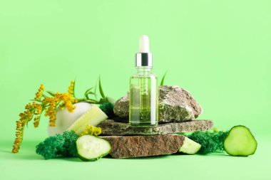 Cosmetic dropper bottle with green moss, cucumber, flowers and rocks on color background