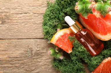 Cosmetic dropper bottle with green moss and grapefruit slices on wooden background
