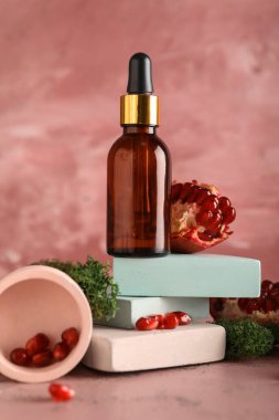 Cosmetic dropper bottle with green moss, pomegranate and decor on pink background