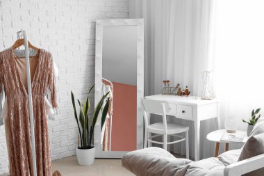 Interior of stylish dressing room with table, mirror and clothes