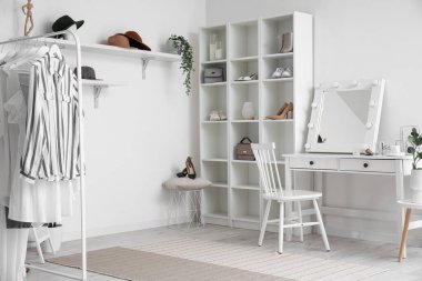 Interior of stylish dressing room with table, shelving unit and clothes
