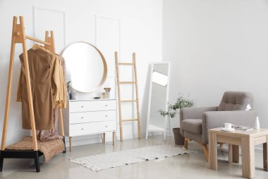 Interior of stylish makeup room with mirrors, clothes and armchair