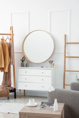 Interior of stylish dressing room with mirror, clothes and drawers