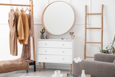 Interior of stylish dressing room with mirror, clothes and drawers