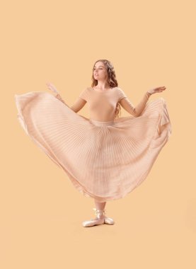 Young ballerina dancing on beige background