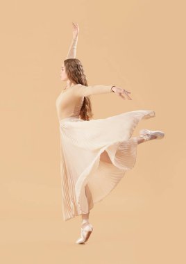 Young ballerina dancing on beige background