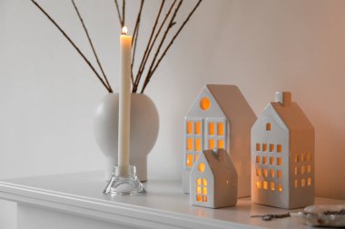House candle holders and vase with tree branches on mantelpiece near light wall