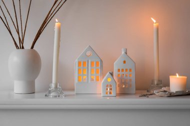 House candle holders and vase with tree branches on mantelpiece near light wall