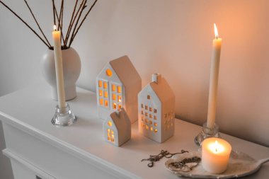 House candle holders and vase with tree branches on mantelpiece near light wall