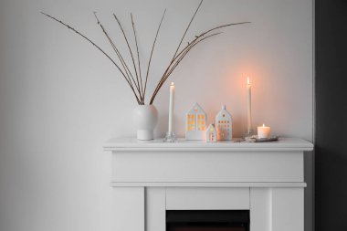 House candle holders and vase with tree branches on mantelpiece near light wall