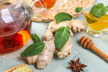 Ginger roots, teapot with black tea, mint leaves and honey on grey table