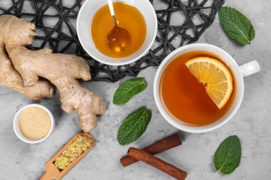 Cup of black tea with lemon, ginger roots, honey and mint leaves on grey table