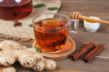 Glass cup of black tea, ginger roots, anise and cinnamon on wooden table