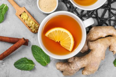 Cup of black tea with lemon, ginger roots, cinnamon and mint leaves on grey table