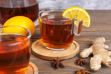 Glass cups of black tea, ginger root, lemon and anise on wooden table